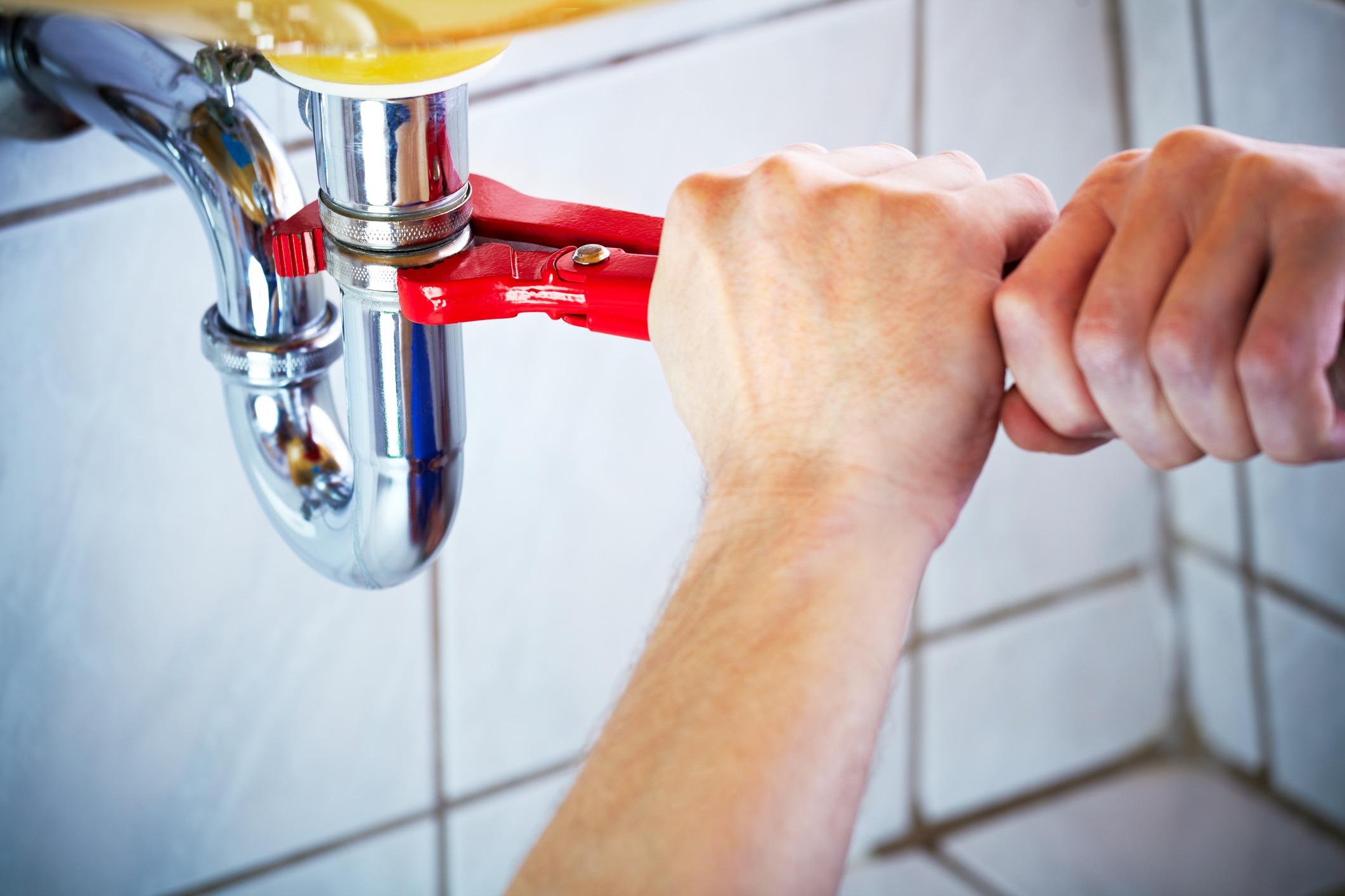 A plumber works on the undercarriage of a sink.