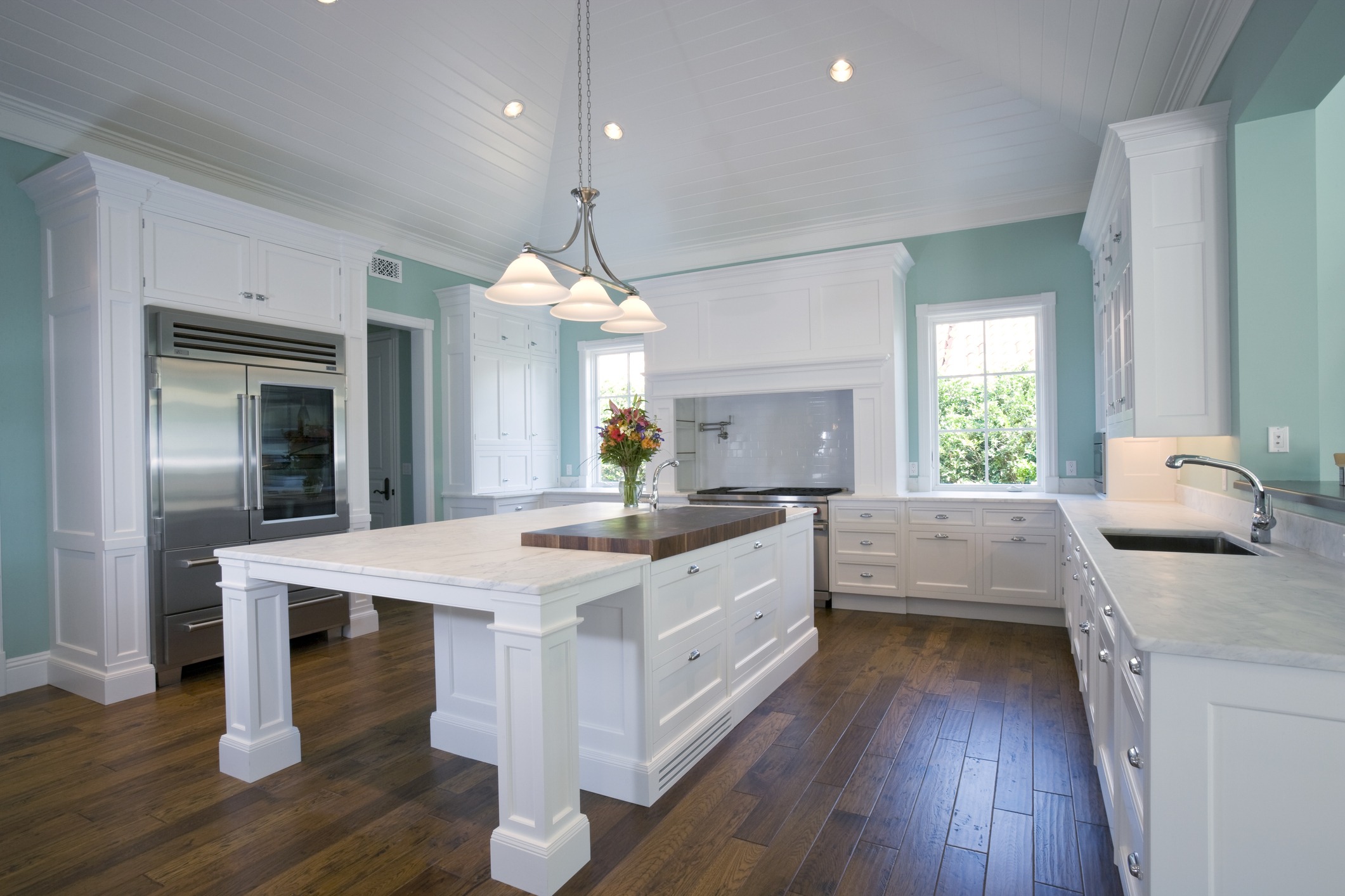 A newly painted kitchen shows off the balance of textures with a wooden floor, glossy white cabinets with a white marble counter to match, and soft teal walls.
