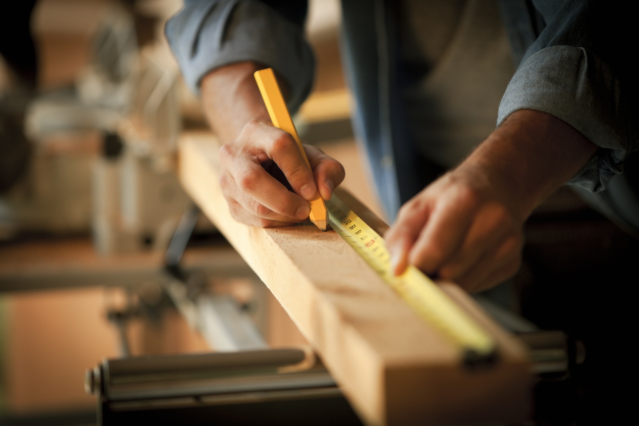 A carpenter measures a wooden plank before cutting it.